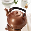 Copper-colored teapot on a white surface with a blurred background